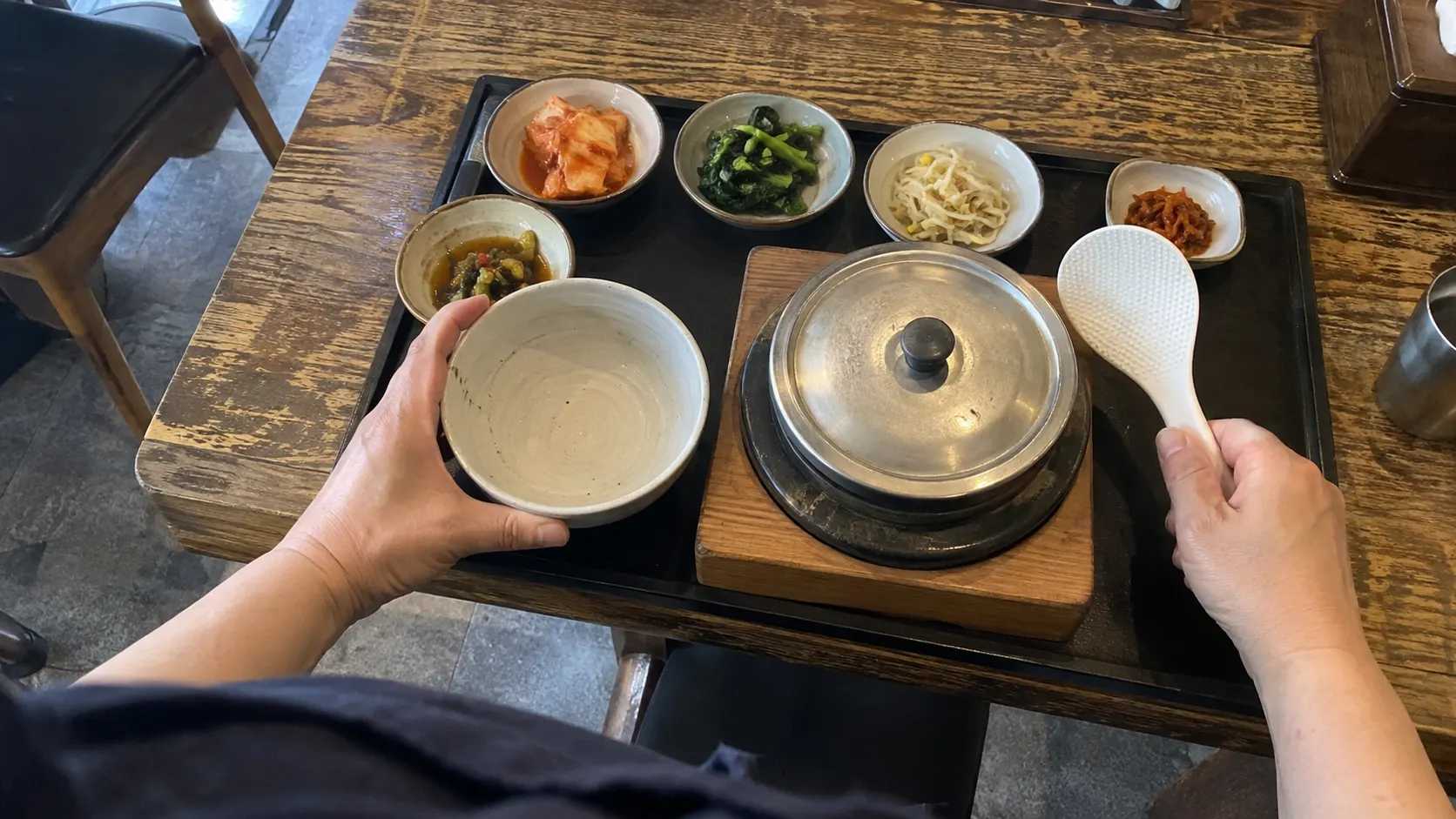 1인용 솥을 올린 쟁반에 빈 공기와 주걱을 배치하고 뚜껑을 내려놓을 자리를 남긴 모습입니다. 밥을 덜 때 손이 지나는 공간과 반찬 그릇 사이의 간격을 실제 상차림에 맞춰 살피는 장면입니다.