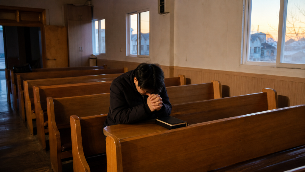 해 뜨기 전 조용한 예배 공간에서 성경을 곁에 두고 기도하는 장면으로 새벽예배의 차분한 분위기를 보여줍니다. — 새벽예배의 기본 의미(새벽예배에 대해 자주 묻는 질문과 알아둘 점) 내용을 보여주는 사진