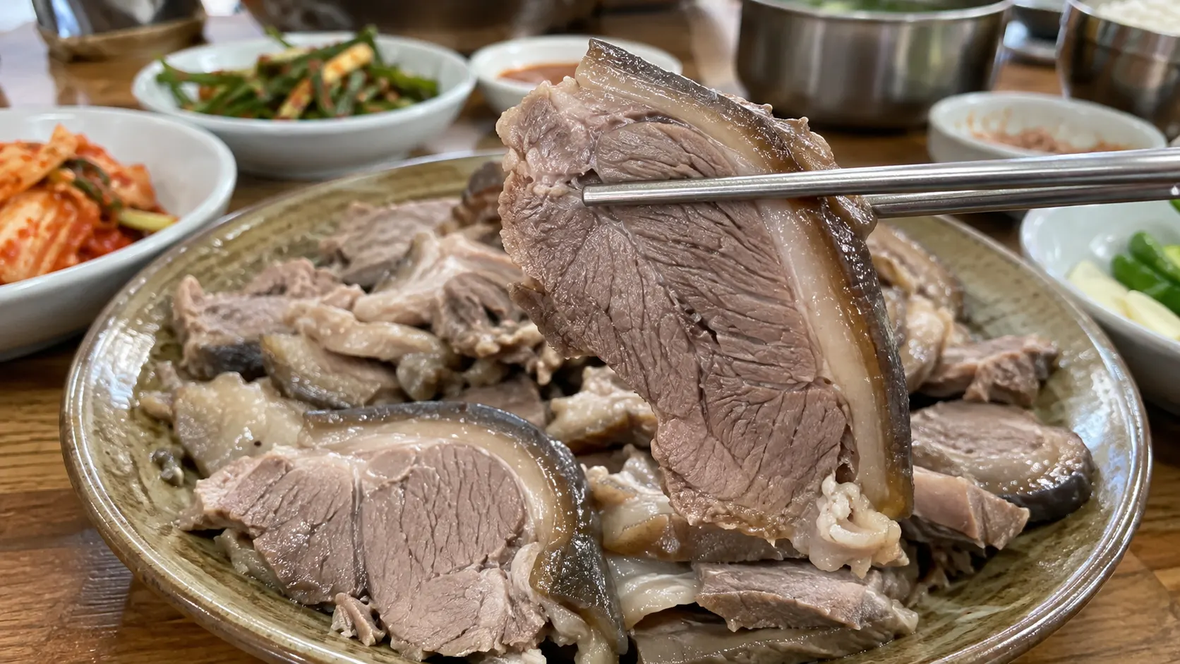 접시에 놓인 흑염소수육을 집어 고기 단면과 두께를 살피는 장면으로, 씹기 어렵다는 느낌을 고기 전체의 문제로 단정하지 않고 어느 부분이 질겼는지 구분하는 기준을 보여줍니다.