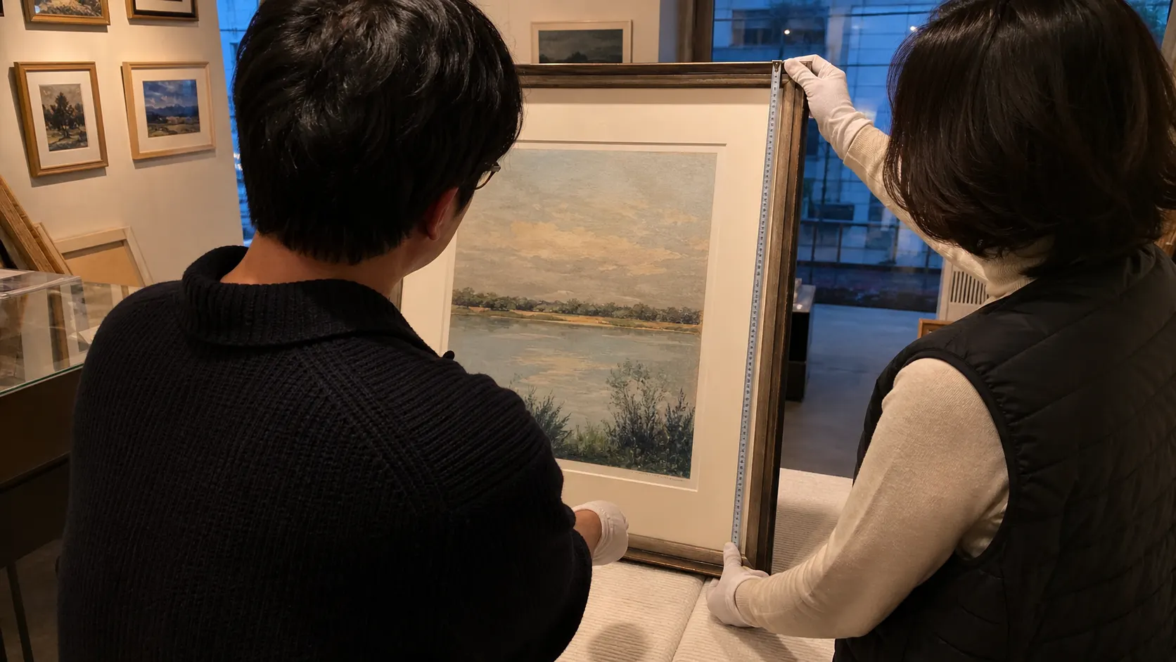 작가와 전시 담당자가 전시장 안에서 장갑을 낀 채 액자 작품의 크기와 표면 상태를 살피며 운송·설치 책임, 작품 목록, 비용 부담, 작품 반환 시점을 대조하는 장면입니다.