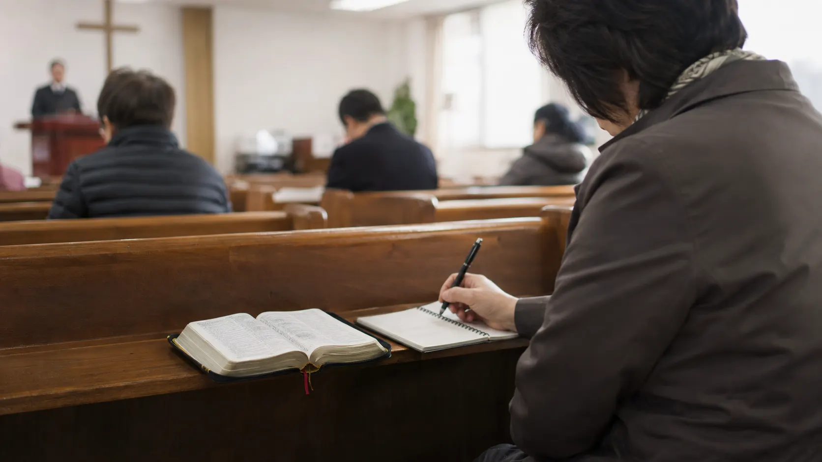 말씀을 듣는 예배에서 성경을 펼친 사람이 설교의 한 문장을 노트에 적고, 주변 회중이 조용히 내용을 따라가는 장면을 보여 줍니다. 적은 문장이 일상 판단의 기준이 되는 흐름을 담습니다.