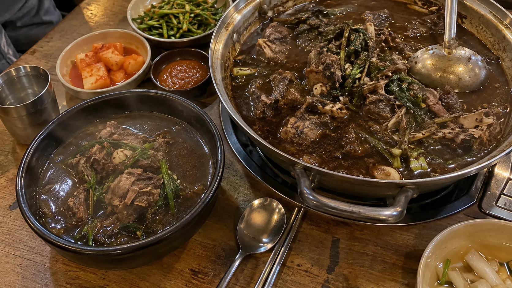 개인 그릇에 담긴 흑염소탕과 여러 사람이 덜어 먹는 전골 냄비를 위에서 바라본 모습입니다. 같은 재료가 한 사람의 식사와 함께 먹는 자리에서 서로 다른 방식으로 제공되는 차이를 보여줍니다.