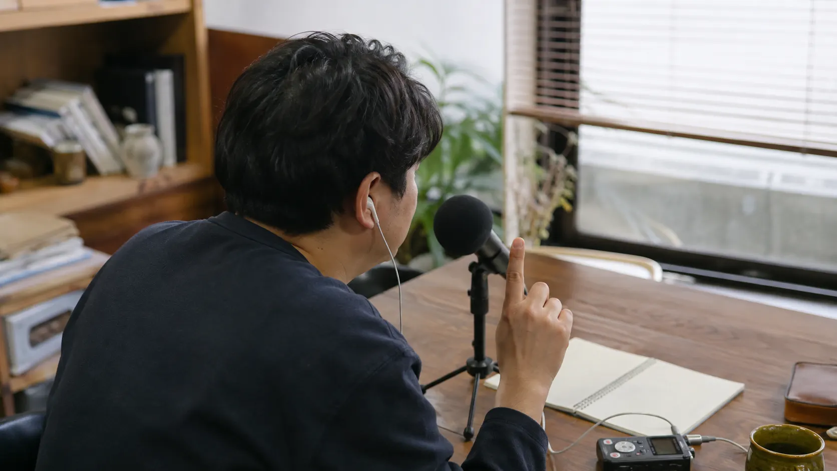 학습자가 이어폰으로 짧은 영어 문장을 들은 뒤 작은 마이크에 대고 따라 말하며 반복 횟수를 손가락으로 표시하는 장면입니다. 소리 듣기와 발화 순서가 드러납니다.