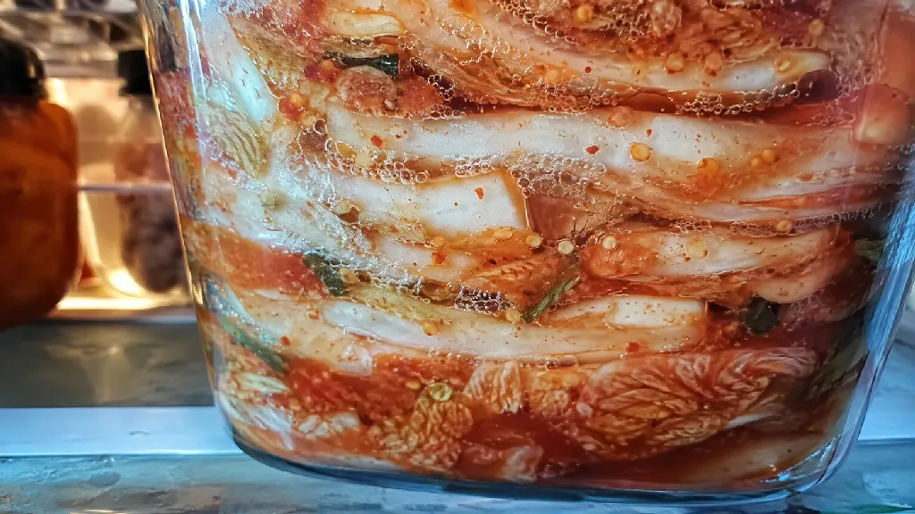 배추 잎과 붉은 양념 사이에 작은 기포가 모이고, 용기를 열 때 발효 과정에서 생긴 탄산가스가 빠져나오는 모습을 설명합니다. 국물의 움직임과 숙성에 따른 산미 변화도 함께 다룹니다.