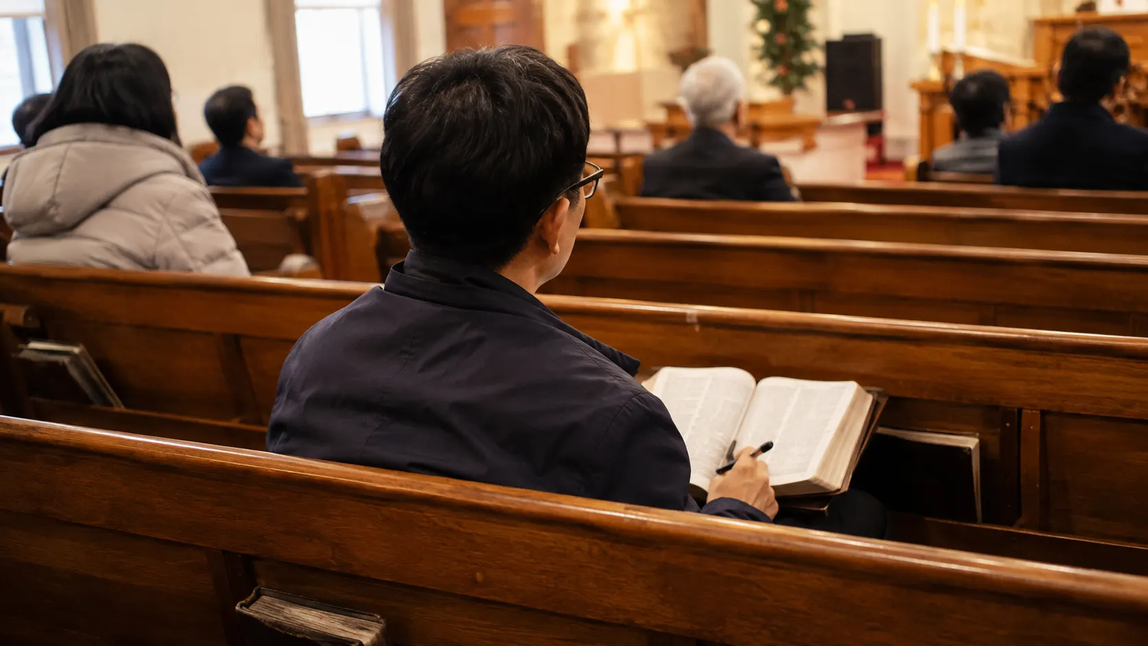 예배 참석자가 열린 성경과 메모장을 곁에 두고 설교를 들으며, 기억할 구절 하나와 예배 뒤 실천할 행동 하나를 차분히 적어 순서를 삶에 연결하는 장면입니다.