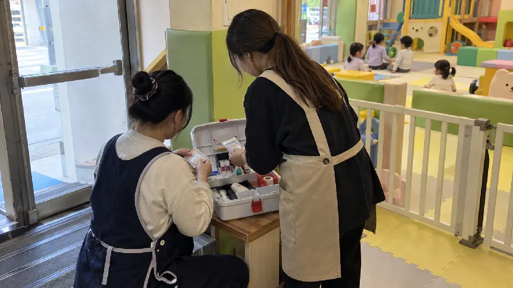 체험 공간 담당자가 구급함과 비상 대피 동선을 살피고, 어린이들이 머무를 활동 구역과 이동 구역을 구분해 예약 전 운영 흐름과 담당자 역할을 함께 확인하는 장면입니다.