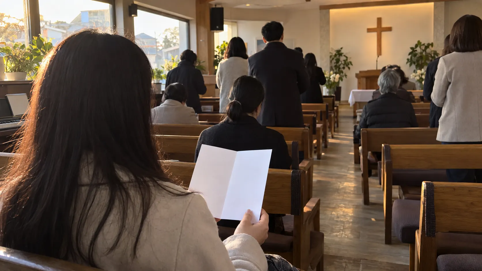 예배 중 참석자들이 안내에 따라 앉고 일어나는 동안 처음 온 사람이 빈 안내지를 보며 흐름을 따라가는 모습입니다. 찬양과 기도 순서의 참여 방식을 보여 줍니다.